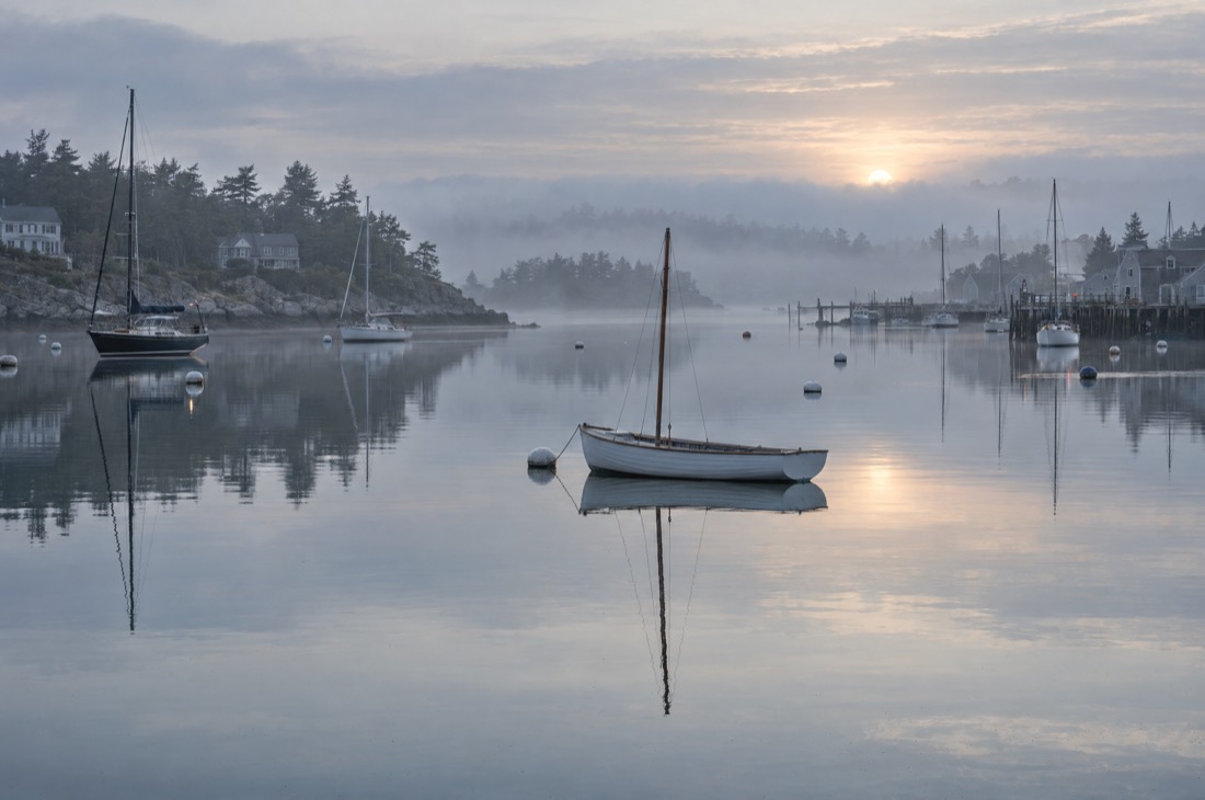 A small harbor at dawn, an empty dinghy drifting on flat calm water